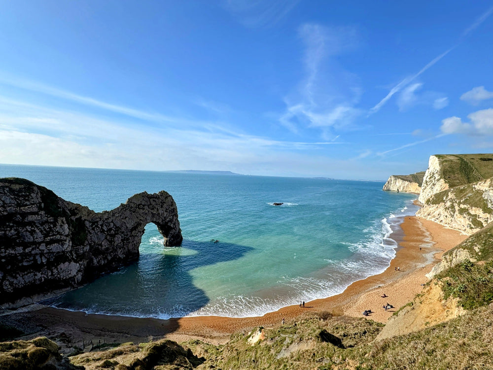 A natural rock arch above a turquoise sea and shingle beach