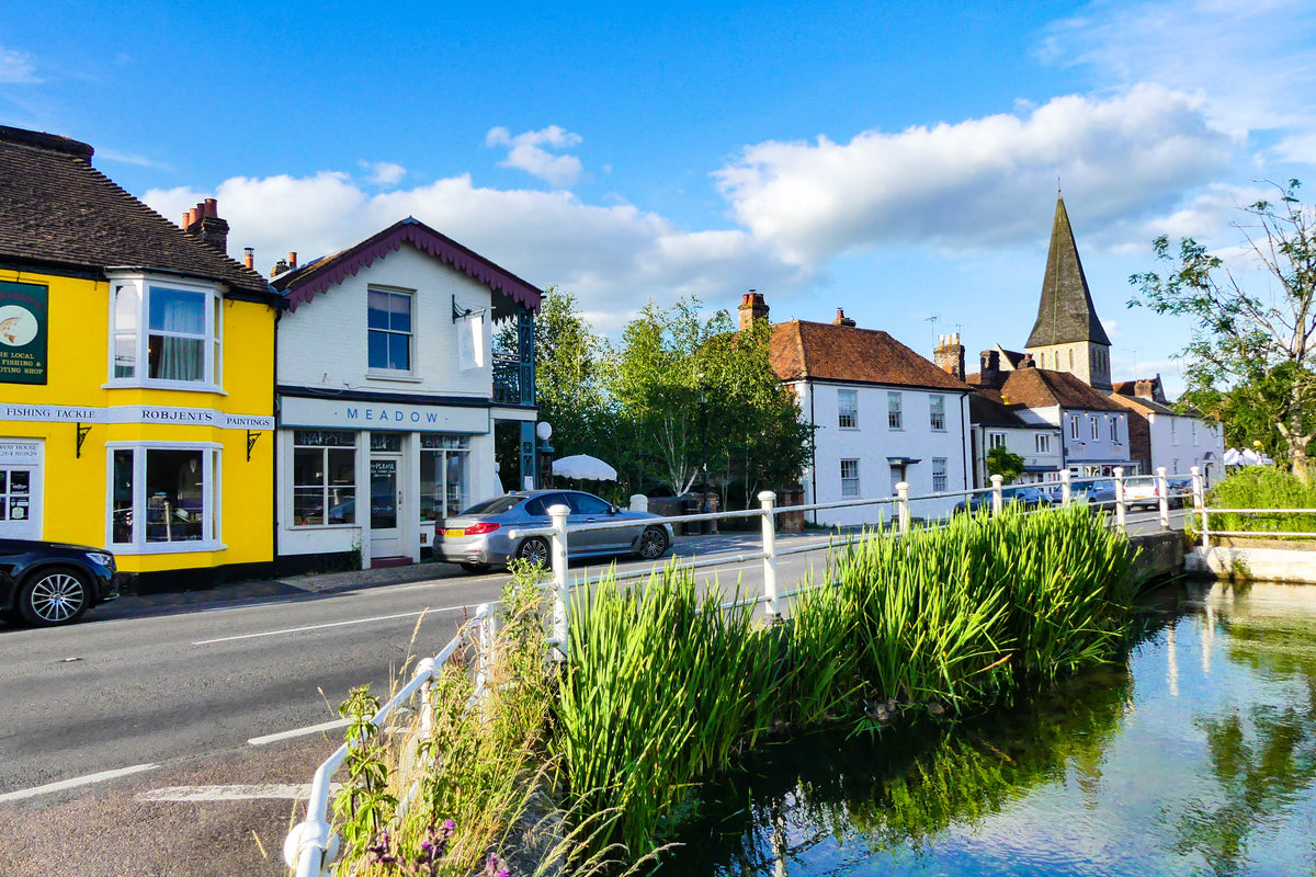 Village shops and a church beside a clear stream under a blue sky