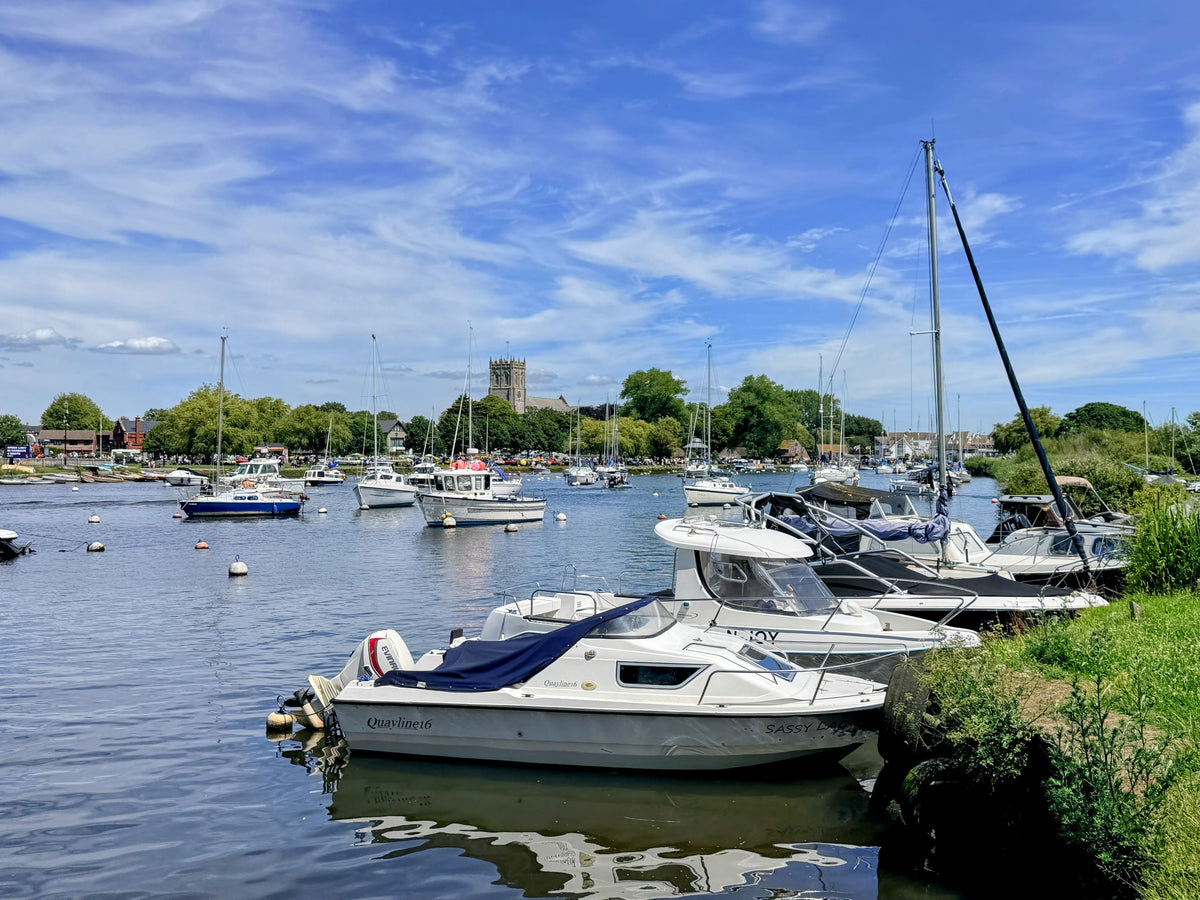 Boats moored in a harbour beside a village and church under a blue sky
